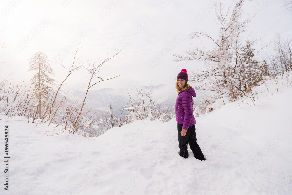 Young woman is standing in  deep snow dressed in colorful clothes and looking at the camera