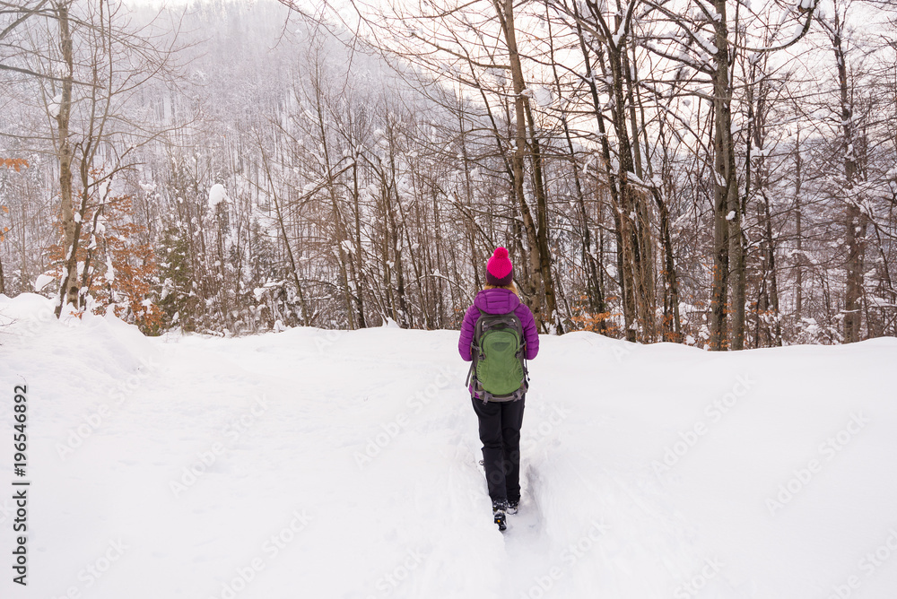 Young woman is walking on the path in deep snow in the forest