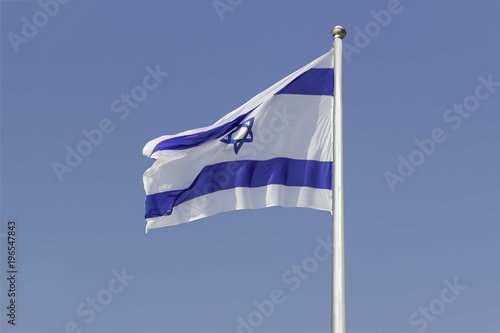 Israel flag flapping in the wind isolated against the blue sky. The flag is on a pole and flapping to the left. there are white clouds in the sky
