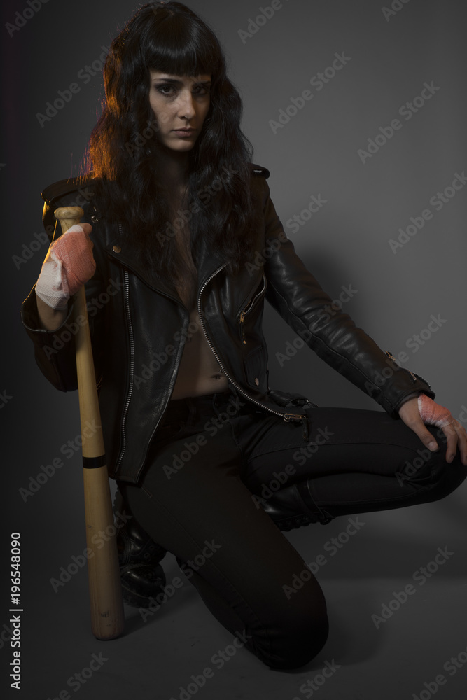 Juvenile delinquency concept, young brunette teenager with black leather jacket and jeans with a baseball bat