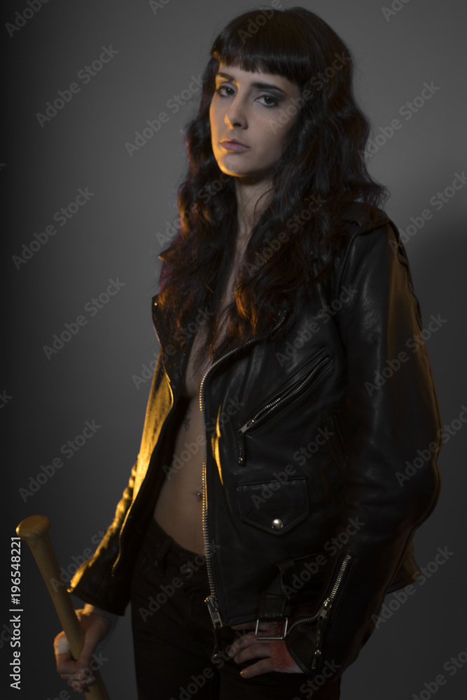 Juvenile delinquency concept, young brunette teenager with black leather jacket and jeans with a baseball bat Juvenile delinquency concept, young brunette teenager with black leather jacket and jeans with a baseball bat