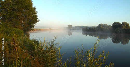 Dawn on the Dnieper River in the summer warm morning. Beautiful landscape, sandy beach and grass against the background of water.