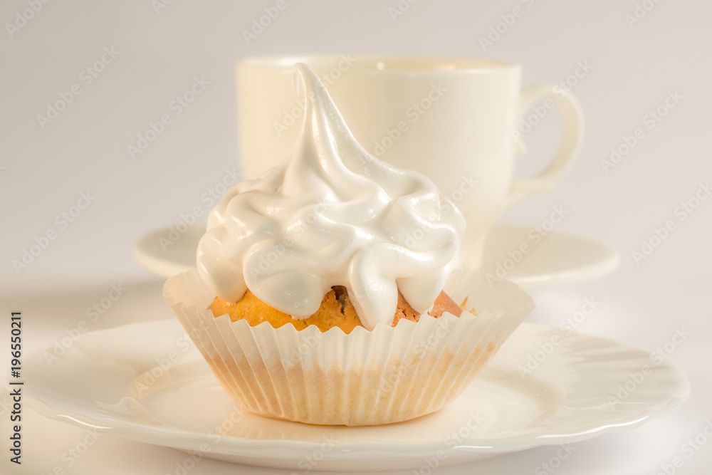 Cupcake with white icing on a plate and a cup of tea. Sweet dessert with white glaze close-up. Cupcake with white icing on a plate and a cup of tea. Sweet dessert with white glaze close-up.