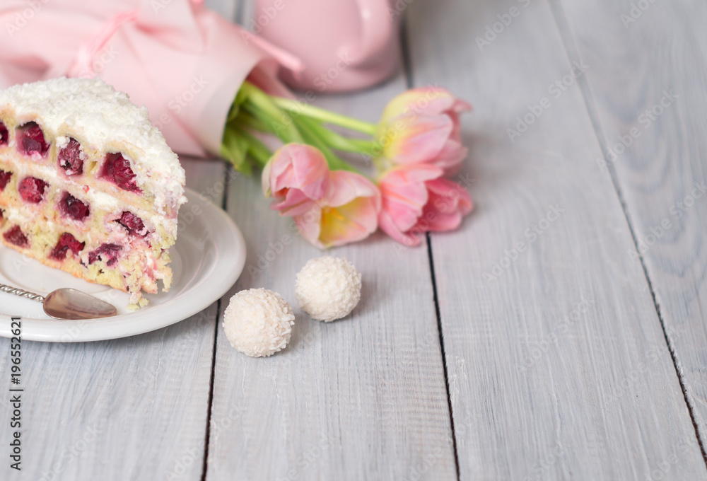 A cake with cherries and pink tulips on white wooden table A cake with cherries and pink tulips on white wooden table