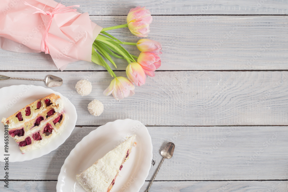 A cake with cherries and pink tulips on white wooden table A cake with cherries and pink tulips on white wooden table
