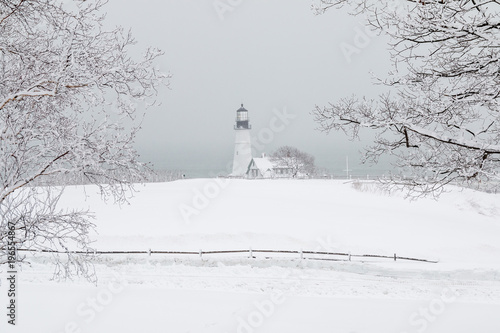 A dreamy snow covered landscape in Maine with a lighthouse in the distance. 