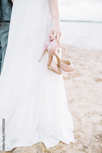 High heel shoes in young woman hands on beach. photo