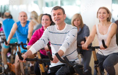 Elderly man on fitness cycle in fitness club.