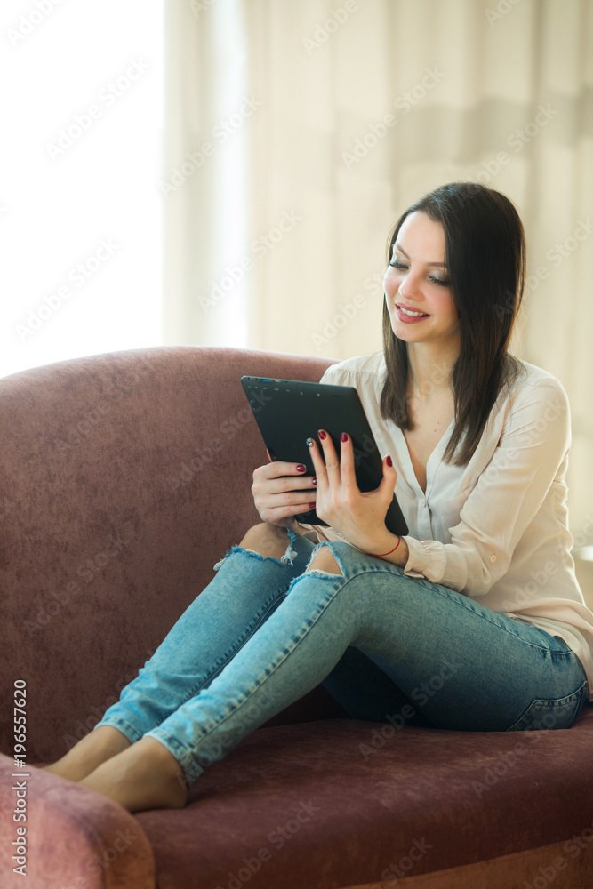 beautiful young girl with dark hair sitting on sofa with tablet beautiful young girl with dark hair sitting on sofa with tablet