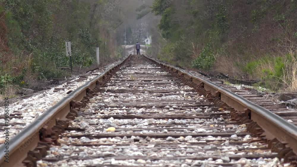 An old black man walks in the distance on lonely railroad tracks.