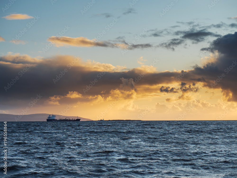 A cargo ship in the ocean at sunset.