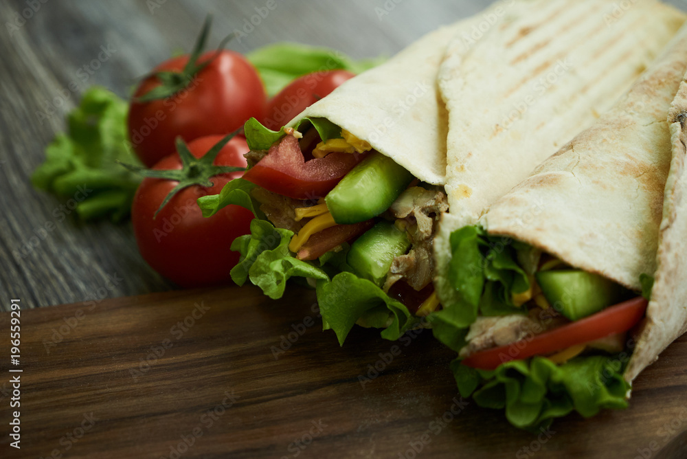 Two Shaurma sandwiches chicken roll in a pita with fresh vegetables tomatoes , cucumber, latitude, cheese and chicken breast meat on wooden cutting board