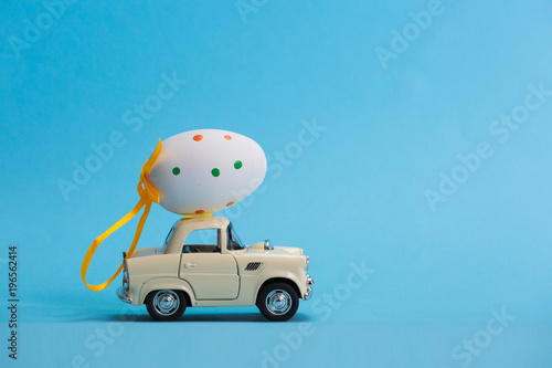 Toy car carrying easter egg isolated on blue background