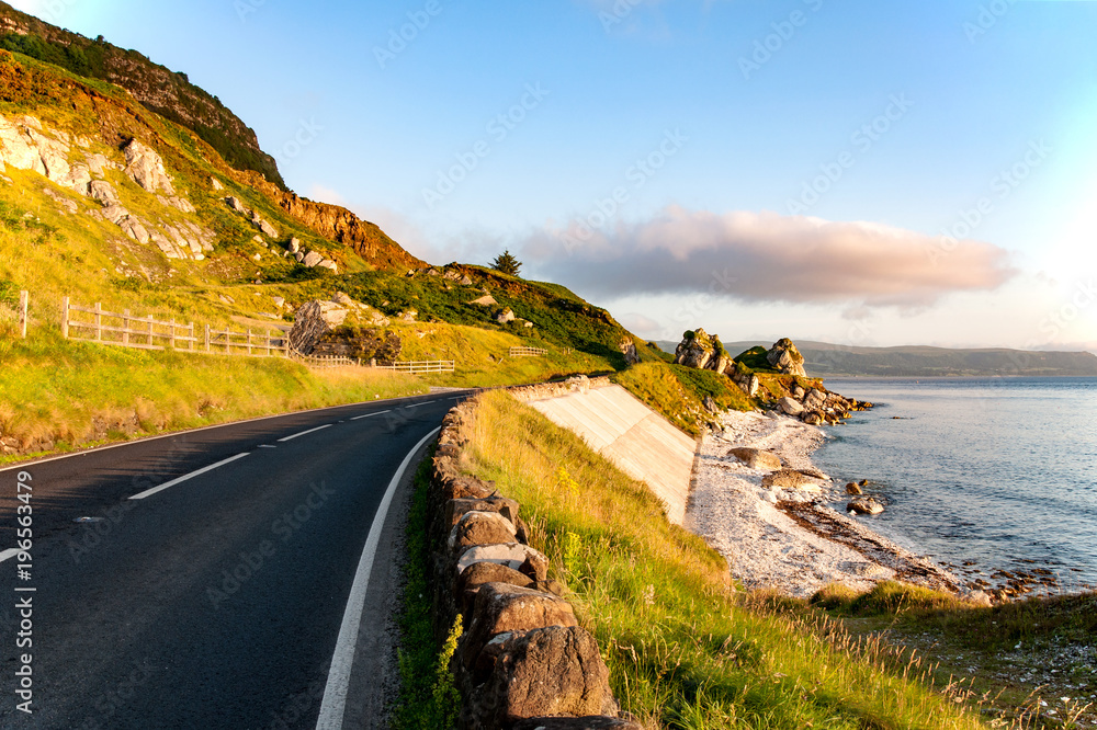 The eastern coast of Northern Ireland and Antrim Coastal road a.k.a. Causeway Coastal Route wit rocks and concrete revetment in sunrise light