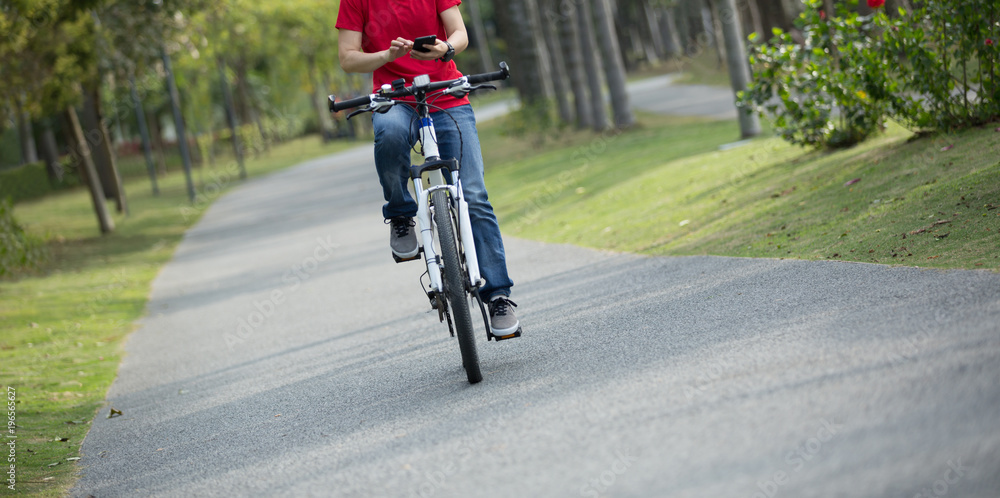 Obraz premium cyclist use cellphone while riding bike in tropical park
