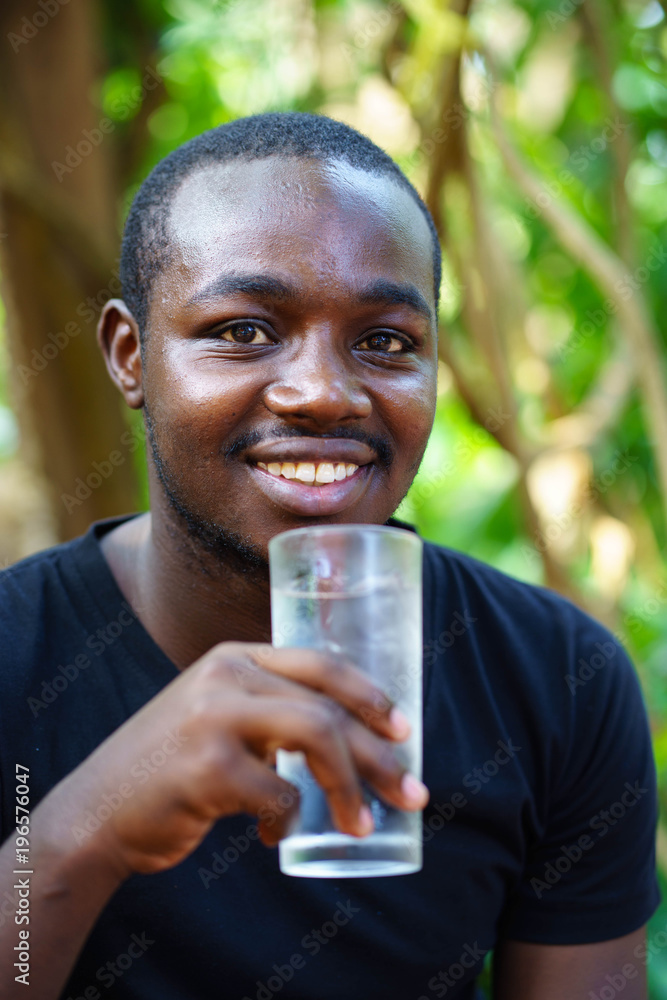 African american man drinking a glass of water with green natural background. African american man drinking a glass of water with green natural background.