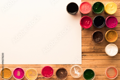 Colorful gouache jars with open caps and blank watercolor paper. Copyspace. Top view