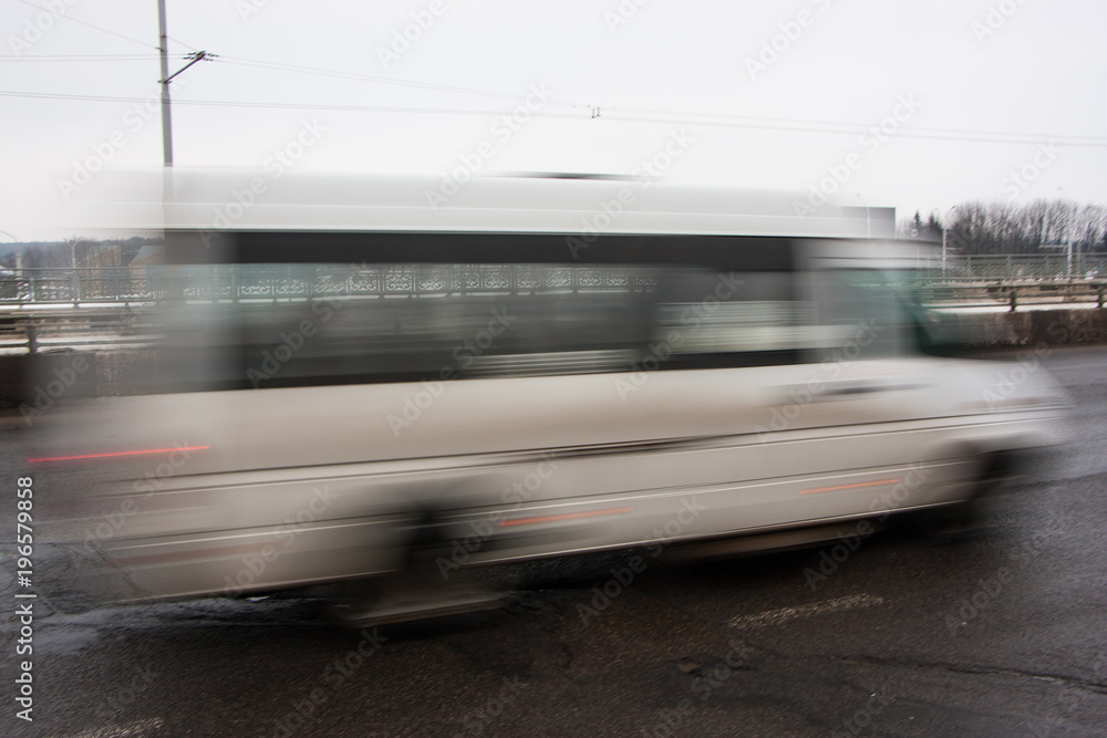 Movement of a blurred white minibus along the highway during the day Movement of a blurred white minibus along the highway during the day