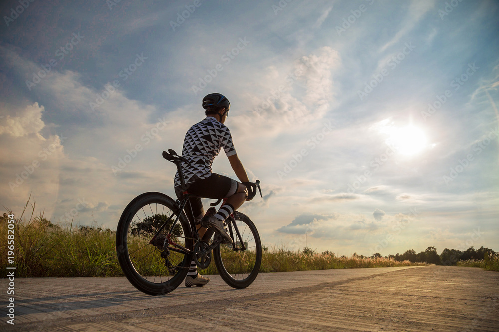 Young man with bicycle on a rural road with grass