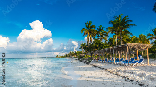 CUBA CAYO: A seat in front of the Caribbean sea. Beautiful beach of Cayo Gulliermo, in Cuba, next to the coral reef, with palm trees and long chairs where to chill out enjoying the breeze and the sun.