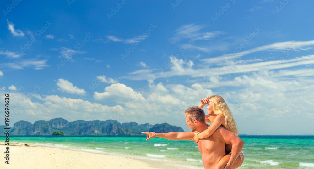 Happy man in love giving piggyback ride to smiling woman at the beach. Couple enjoying vacation at beach
