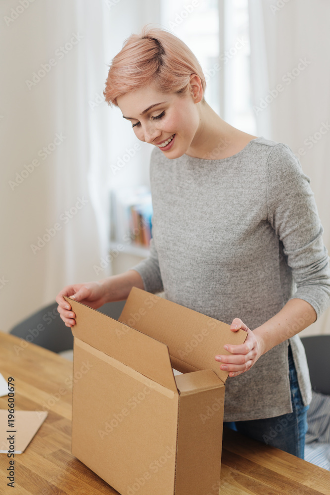 Pleased young woman opening a cardboard box