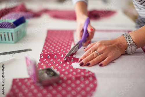 young woman seamstress making pattern on fabric with tailors chalk. Girl working with a sewing pattern. Hobby sewing as a small business concept. Tailor measuring textile material