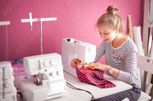 Smiling seamstress and her hand close up in workshop. Young dressmaker woman sews clothes on sewing machine.