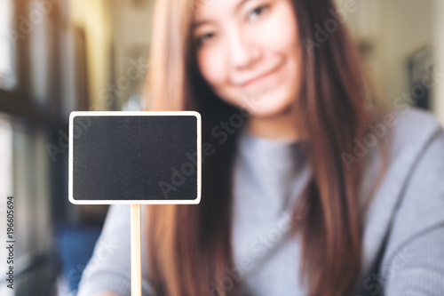 A beautiful asian woman holding a blank square blackboard sign with blur background