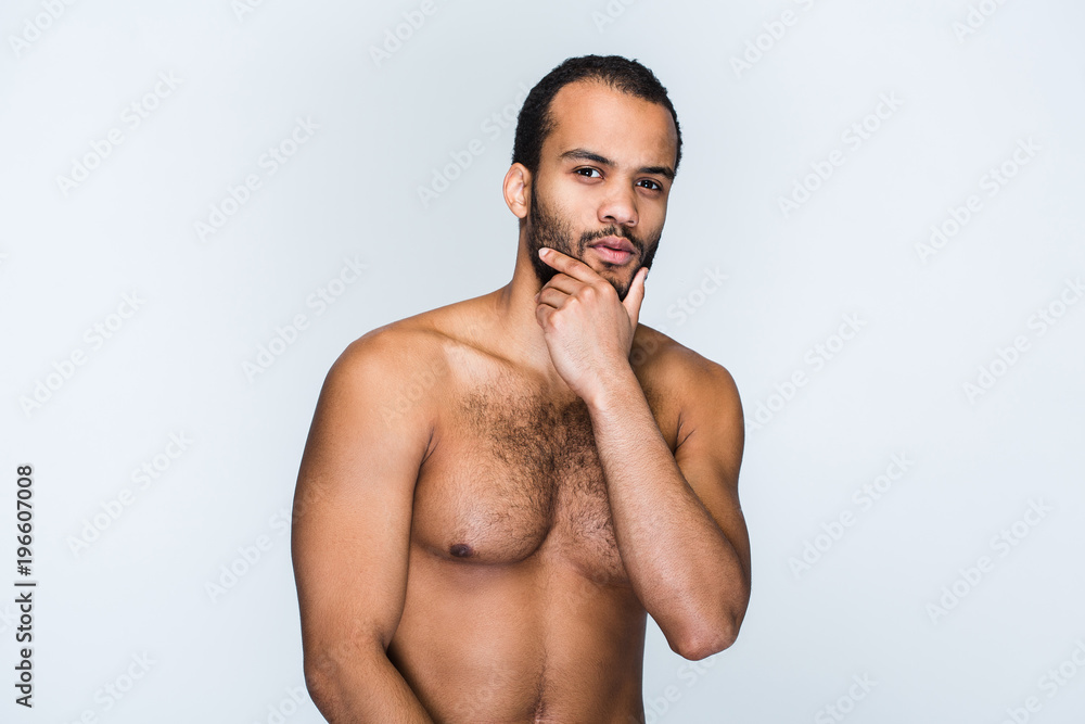 Handsome and confidant. Portrait of handsome shirtless young black man keeping hand on chin and looking at camera while standing against white background Handsome and confidant. Portrait of handsome shirtless young black man keeping hand on chin and looking at camera while standing against white background