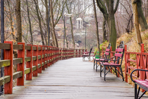 Wallpaper Mural Wooden path - hinged bridge with wet boards, wrought iron benches and lanterns in the park on a hillside overlooking the white rotunda and granite stones in the background. Autumn rainy wet landscape Torontodigital.ca