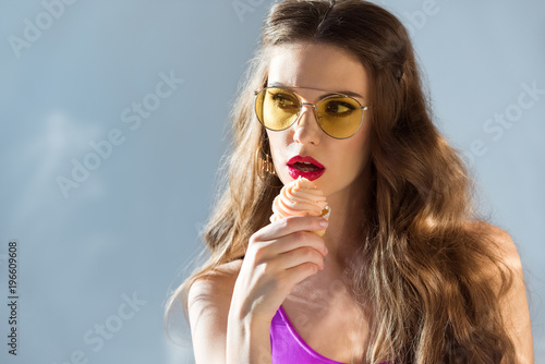 sexy attractive girl in ultra violet swimsuit and sunglasses eating cupcake on grey