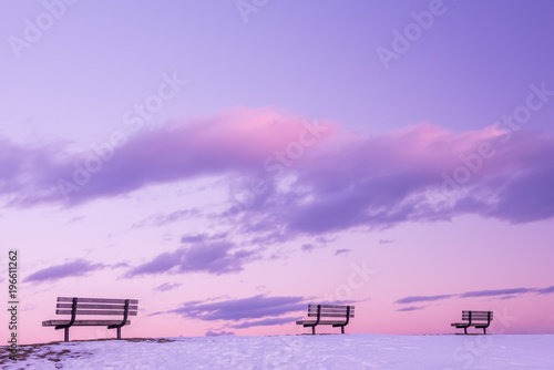 Photo A series of benches against the background of a gentle pink sky with clouds