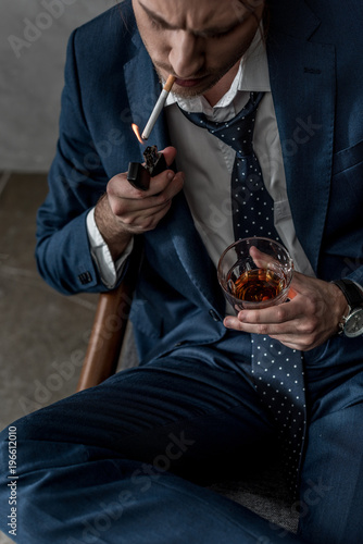 high angle view of businessman with glass of whiskey smoking cigarette