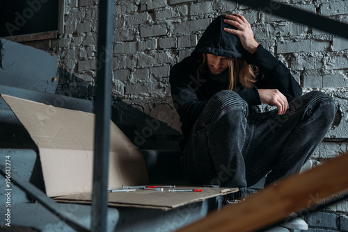 Foto heroin addicted junkie sitting on stairs with syringes