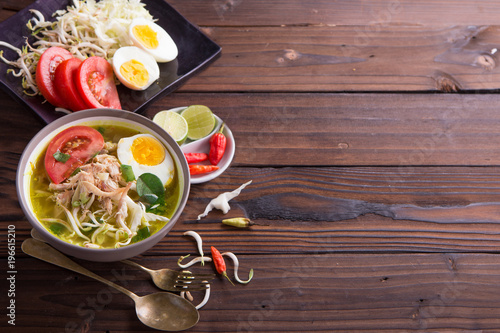 Soto: Indonesian chicken soup with hard boiled eggs, tomato, bean sprout, lemon, cayenne pepper on rustic brown wooden background photo