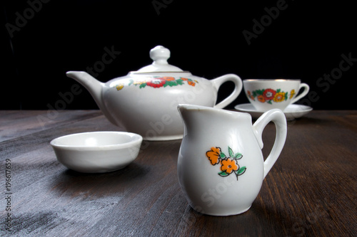 White ceramic tea pot with floral pattern on wooden table with cup of tea