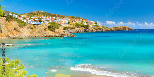 Fototapeta Naklejka Na Ścianę i Meble -  Sunny sandy Livadi beach in sea Bay of resort village Bali. Sea waves wash the sandy beach. View of rocky coast with white houses. Bali, Rethymno, Crete, Greece