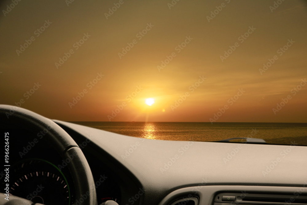 Dark car Interior - steering wheel, shift lever and dashboard. Car modern inside. Front view on sunset and sea background. The sun shines in the glass. glare