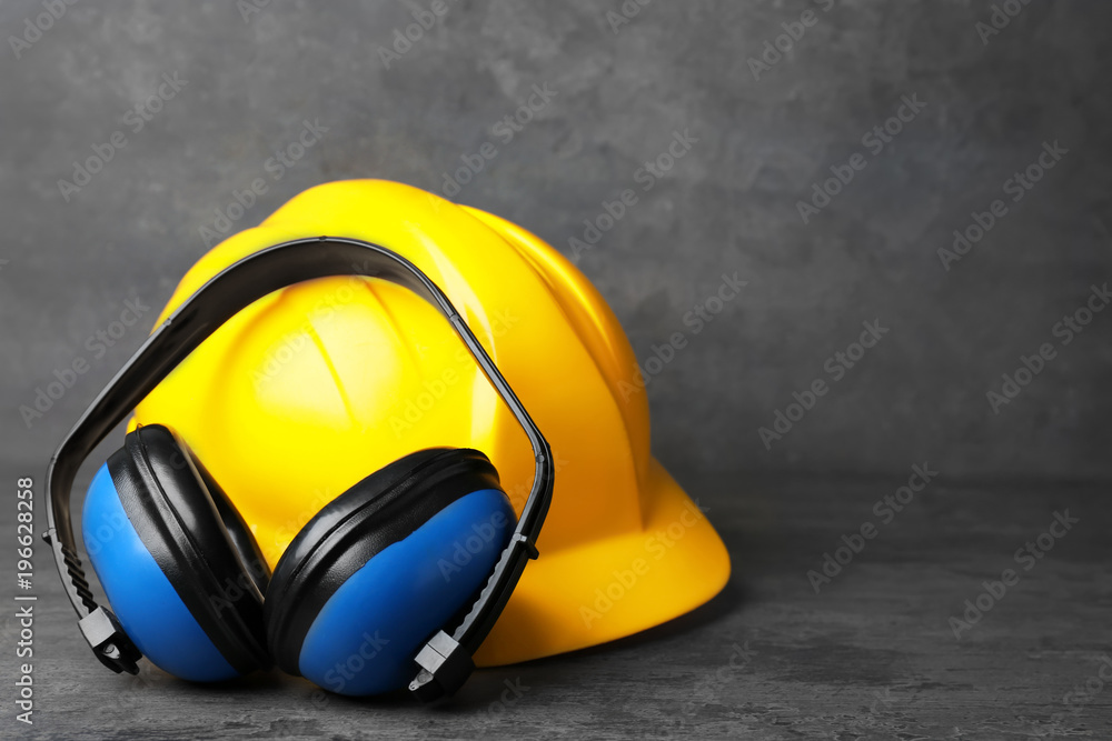 Headphones and hard hat on table against grey background. Hearing protection  equipment Stock Photo | Adobe Stock