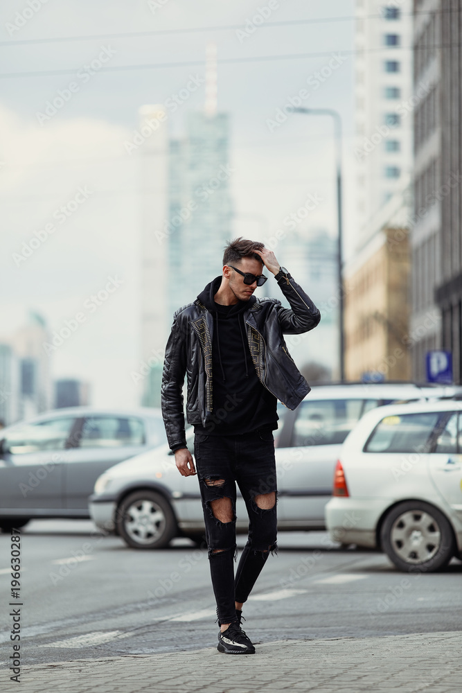 Model looking man stand on the city street with cars background, look on his watch and around Model looking man stand on the city street with cars background, look on his watch and around