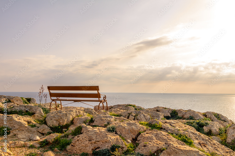Bench on a rock in the popular tourist destination on the background of a romantic sunset, Cape Greco, Cyprus