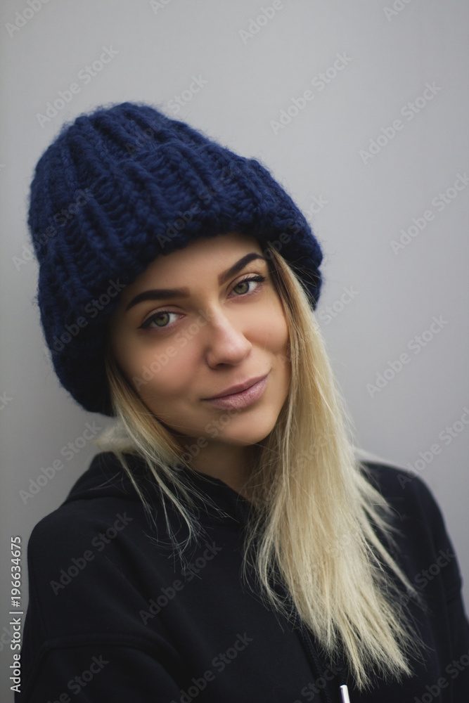 a blonde girl with big eyes and plump lips against a light gray background. woman in a voluminous warm dark blue cap a blonde girl with big eyes and plump lips against a light gray background. woman in a voluminous warm dark blue cap
