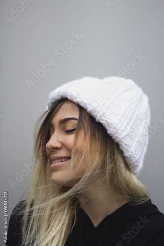 blonde girl with big eyes and plump lips against a light gray background. woman in a volumetric warm white hat.