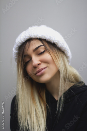 blonde girl with big eyes and plump lips against a light gray background. woman in a volumetric warm white hat.