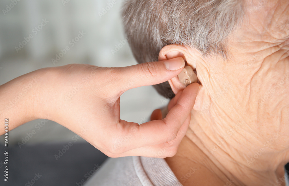 Doctor putting hearing aid in senior woman's ear indoors