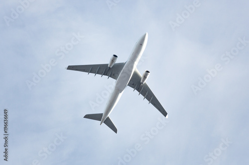 Travel, transportation, aviation concept, copy space/ Wide-body passenger airplane  flying overhead against a spring blue sky, bottom view