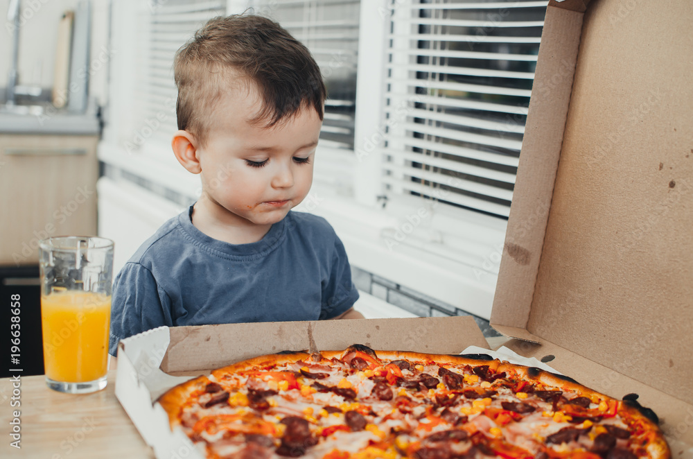 the little boy eats a huge harmful pizza himself in the kitchen and drinks juice, very fat and harmful the little boy eats a huge harmful pizza himself in the kitchen and drinks juice, very fat and harmful
