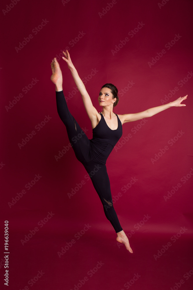 Beautiful slim flexible woman is wearing black body costume in studio isolated on red