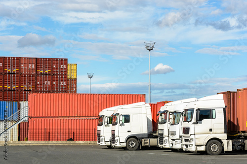 Fototapeta Naklejka Na Ścianę i Meble -  A row of white semi-trailer trucks parked on the parking lot of a container storage platform in the intermodal terminal of a river port.